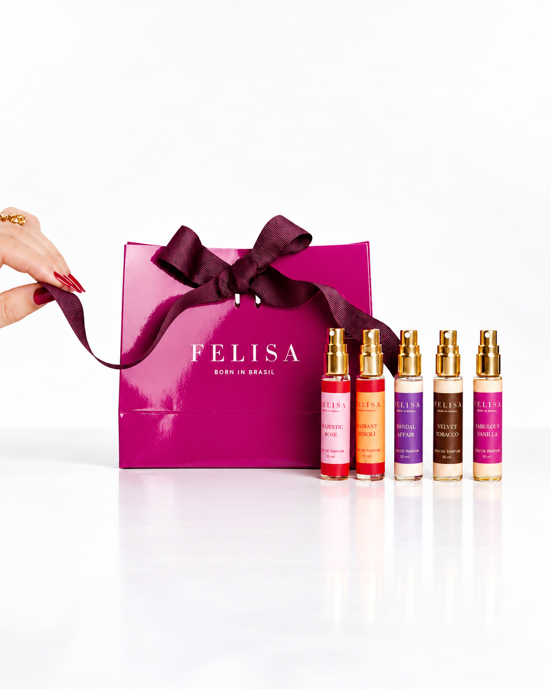 Miniaturas de 10 ml dos perfumes Majestic Rose, Fabulous Vanilla, Sandal Affair, Velvet Tobacco e Radiant Neroli em pé, sem tampas, ao lado de uma sacola roxa da Felisa com laço sendo aberto por uma mão