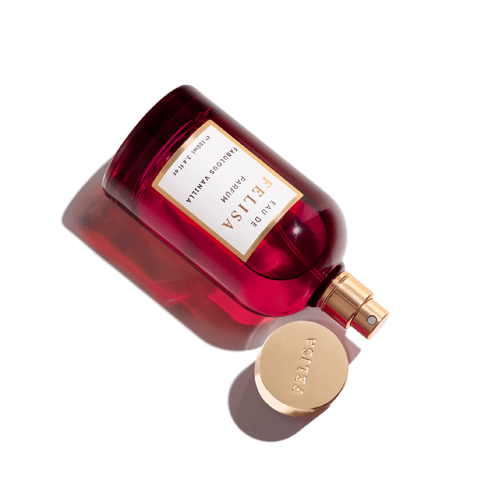 Frasco de Fabulous Vanilla Eau de Parfum na cor vermelha intensa, deitado sobre fundo branco, com a tampa dourada ao lado